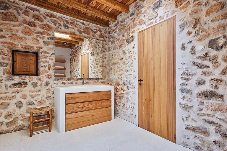 Baño rústico con mobiliario de madera a medida y puerta maciza en finca de lujo Can Pilot en Ibiza