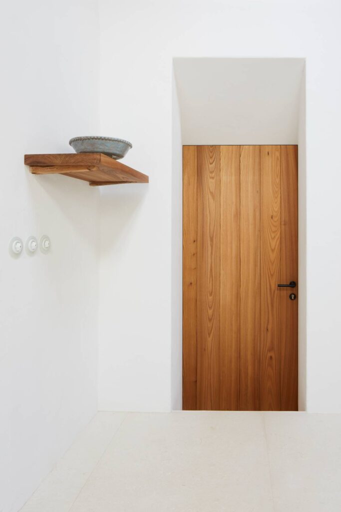 Puerta de madera natural a medida instalada en pared blanca
