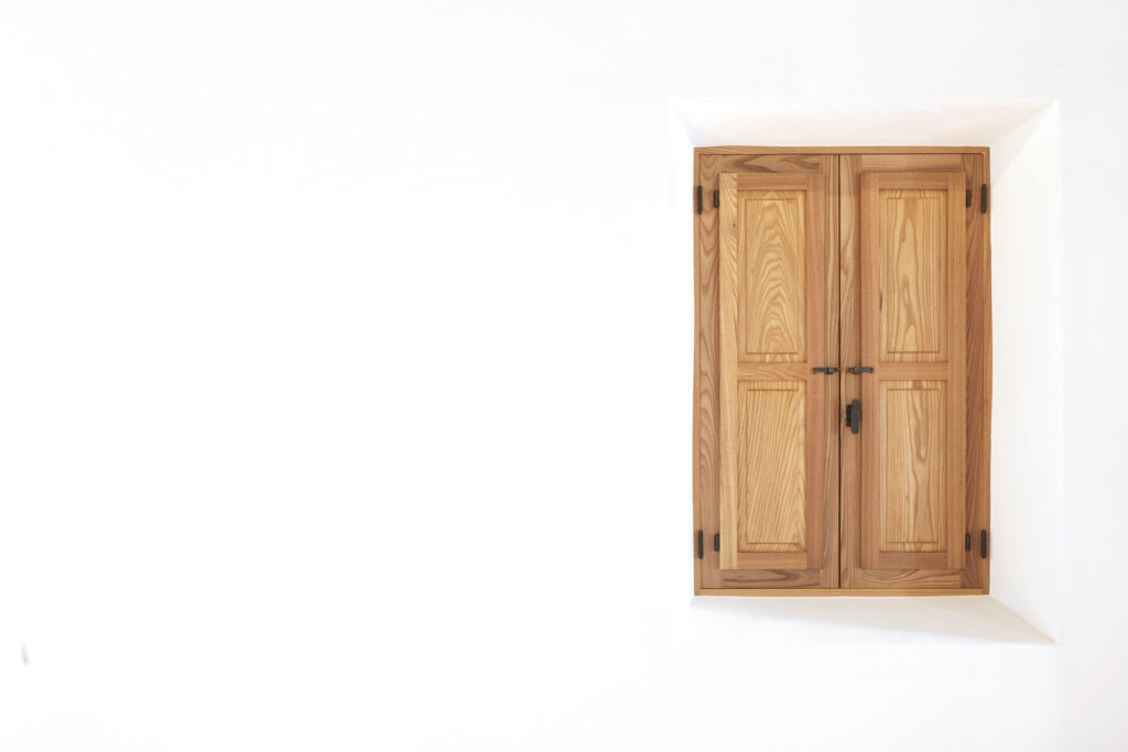 Ventana mallorquina con postigos de madera maciza instalada por Carpintsa en vivienda de estilo ibicenco